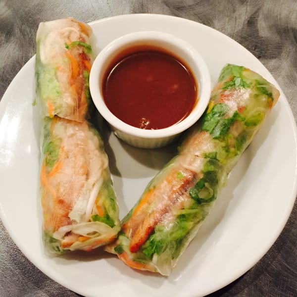 Two fresh Vietnamese spring rolls with shrimp, vegetables, and a side of dipping sauce.