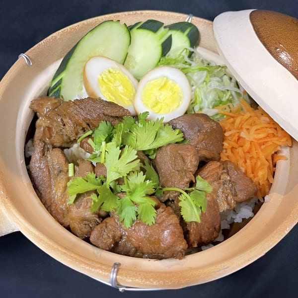 Vietnamese clay pot with braised pork, rice, sliced cucumbers, boiled eggs, shredded carrots, and cilantro.
