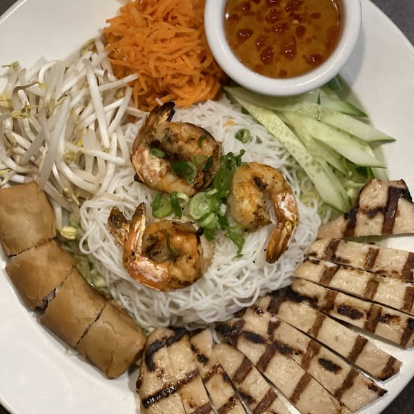 Vietnamese vermicelli bowl with grilled shrimp, sliced chicken, egg rolls, and fresh vegetables.
