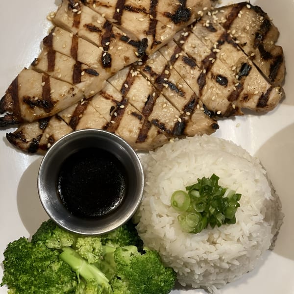 Grilled chicken with sesame seeds, white rice topped with green onions, steamed broccoli, and a side of sauce.
